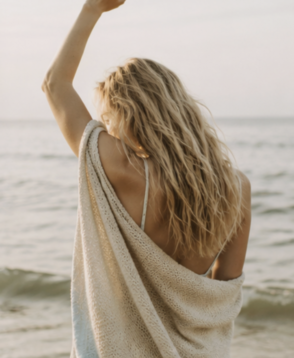 A woman wrapped in a knit blanket on the beach at sunrise, calm and present